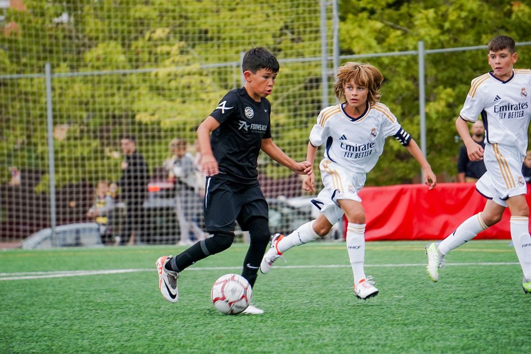 Forms Academy player drives at two defenders during a youth match in Madrid